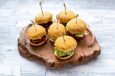 Slider burgers sitting on a wooden serving board