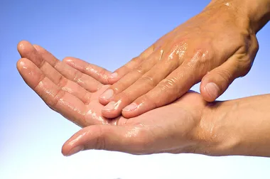 Rubbing alcohol being applied to hands with a light blue to white gradient in the background
