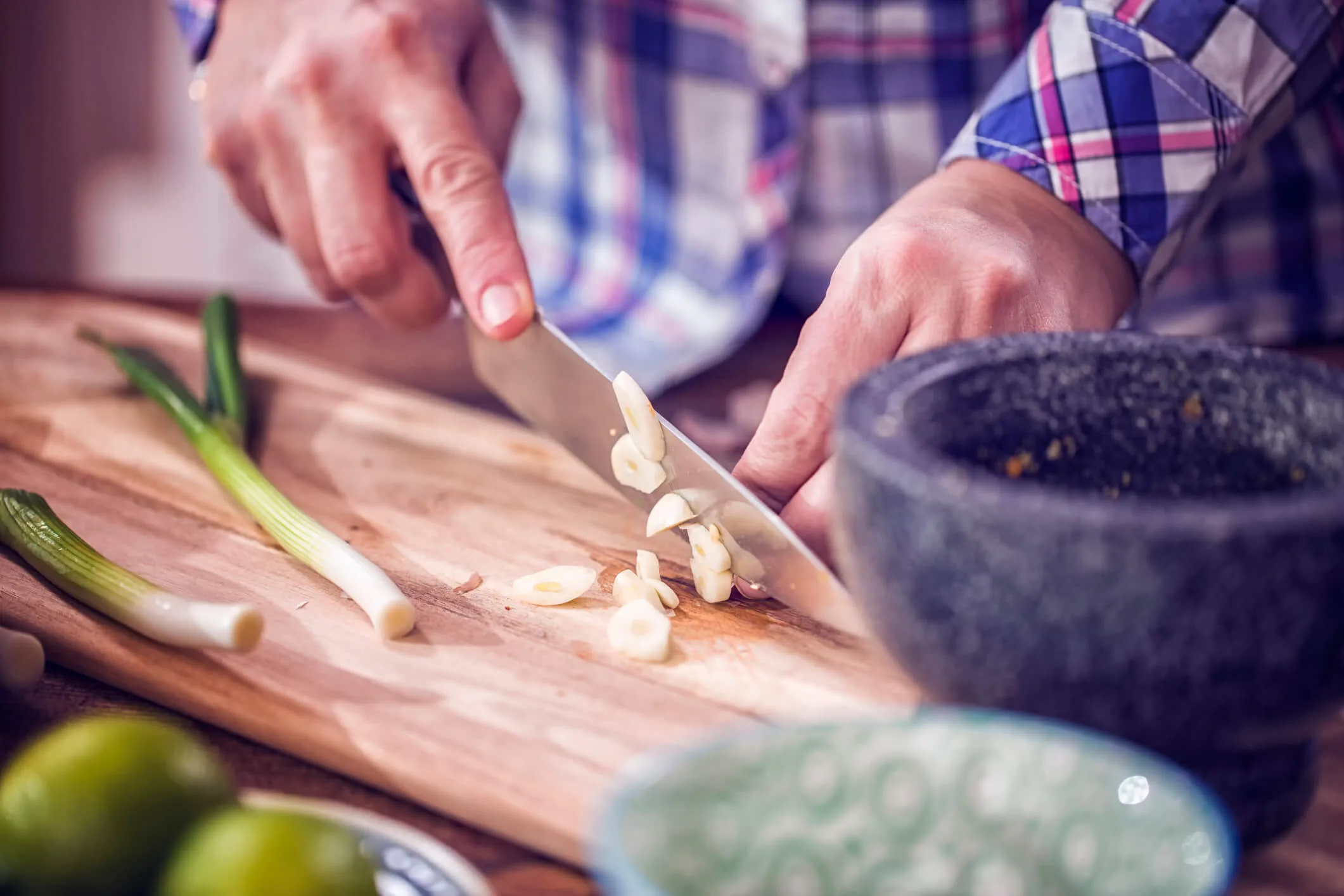 An elderly man chopping spring onion and garlic on a wooden chopping board