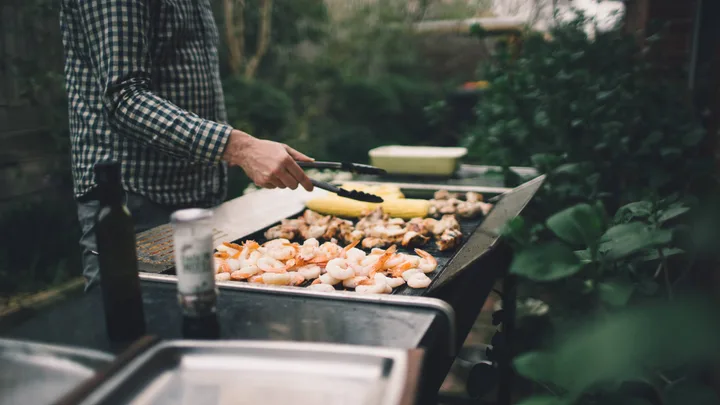 A man barbecuing vegetables and seafood at a family bbq