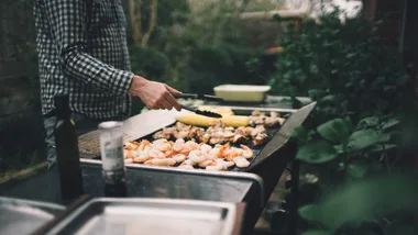 A man barbecuing vegetables and seafood at a family bbq