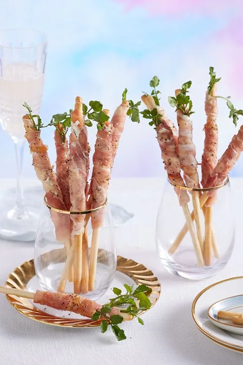 Grissini sticks in stemless wine glasses with gold bordered plate underneath