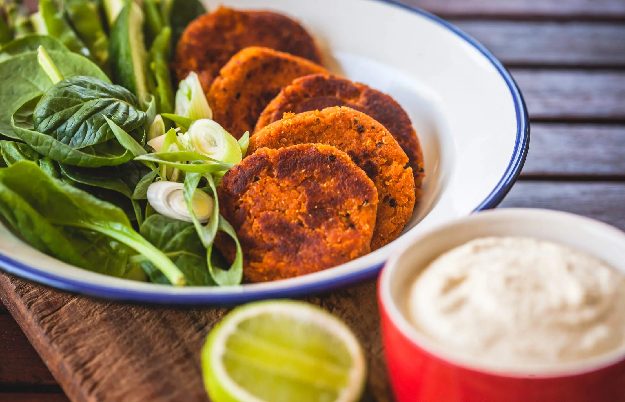 Red lentil and quinoa patties in a bowl with green leafy vegetables