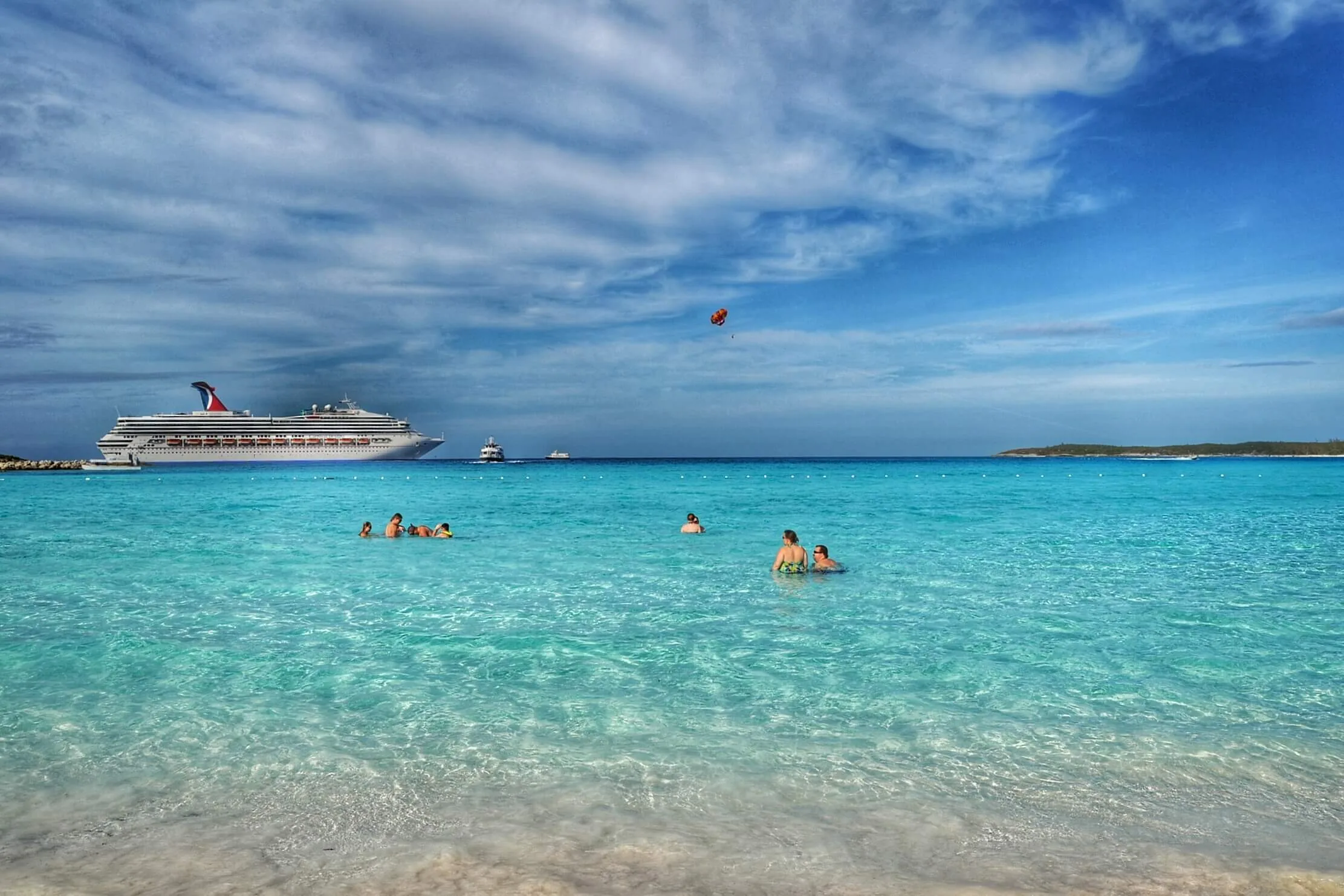 People swimming at the beach in front of a cruise ship