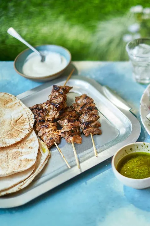 Sticky jerk lamb kebab skewers with flatbread on the side and sauce in the background