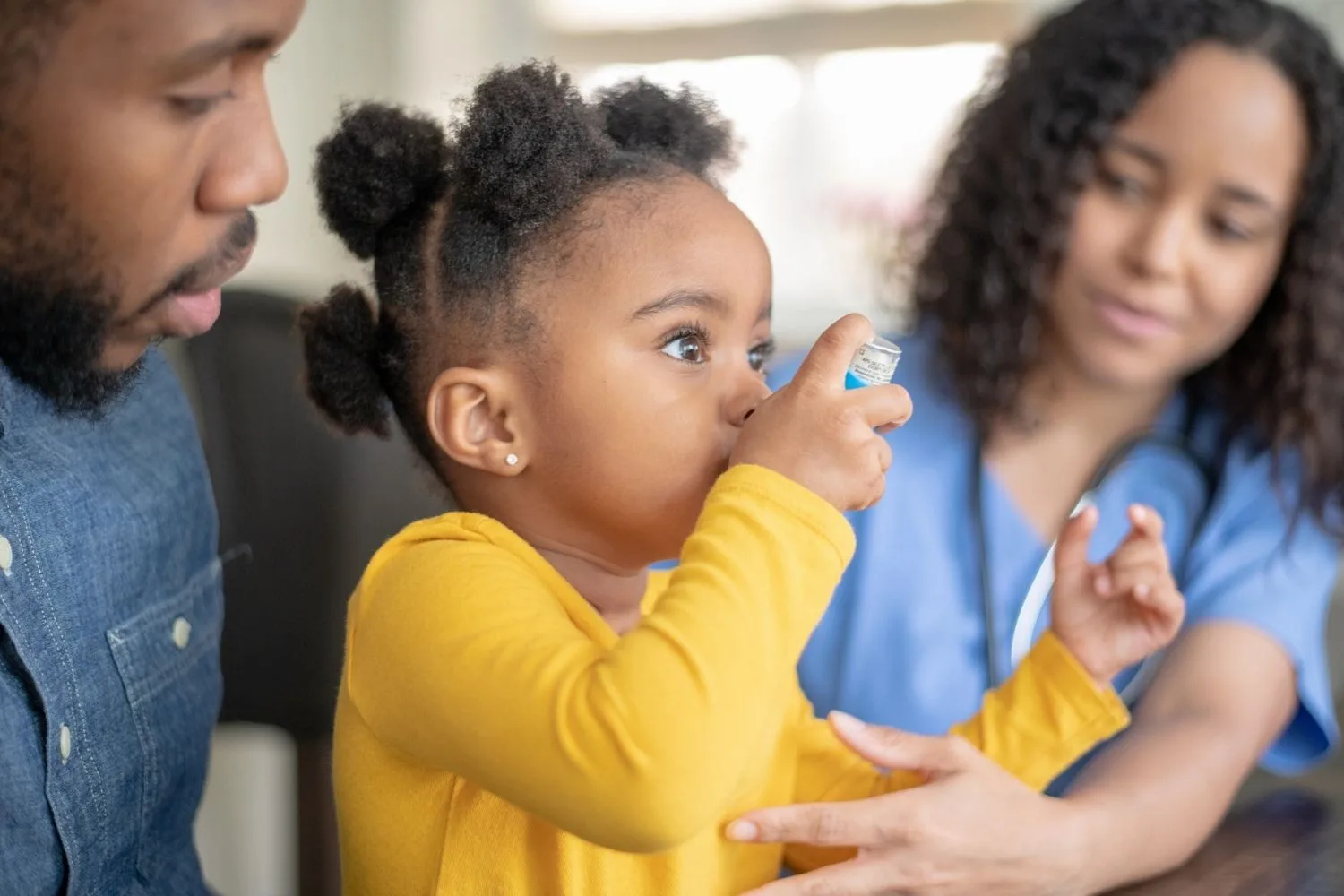 little girl using asthma pump with dad and doctor