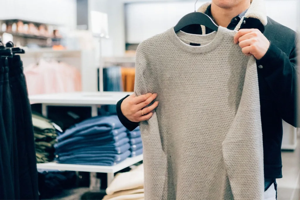 Man holding grey jumper in clothing shop