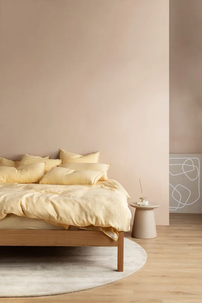 Timber bed with yellow linen in a peach-coloured room