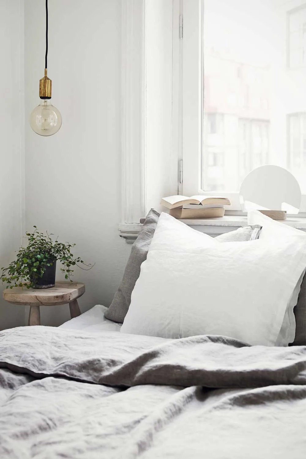 Bed with grey and white linen sheets beneath a window