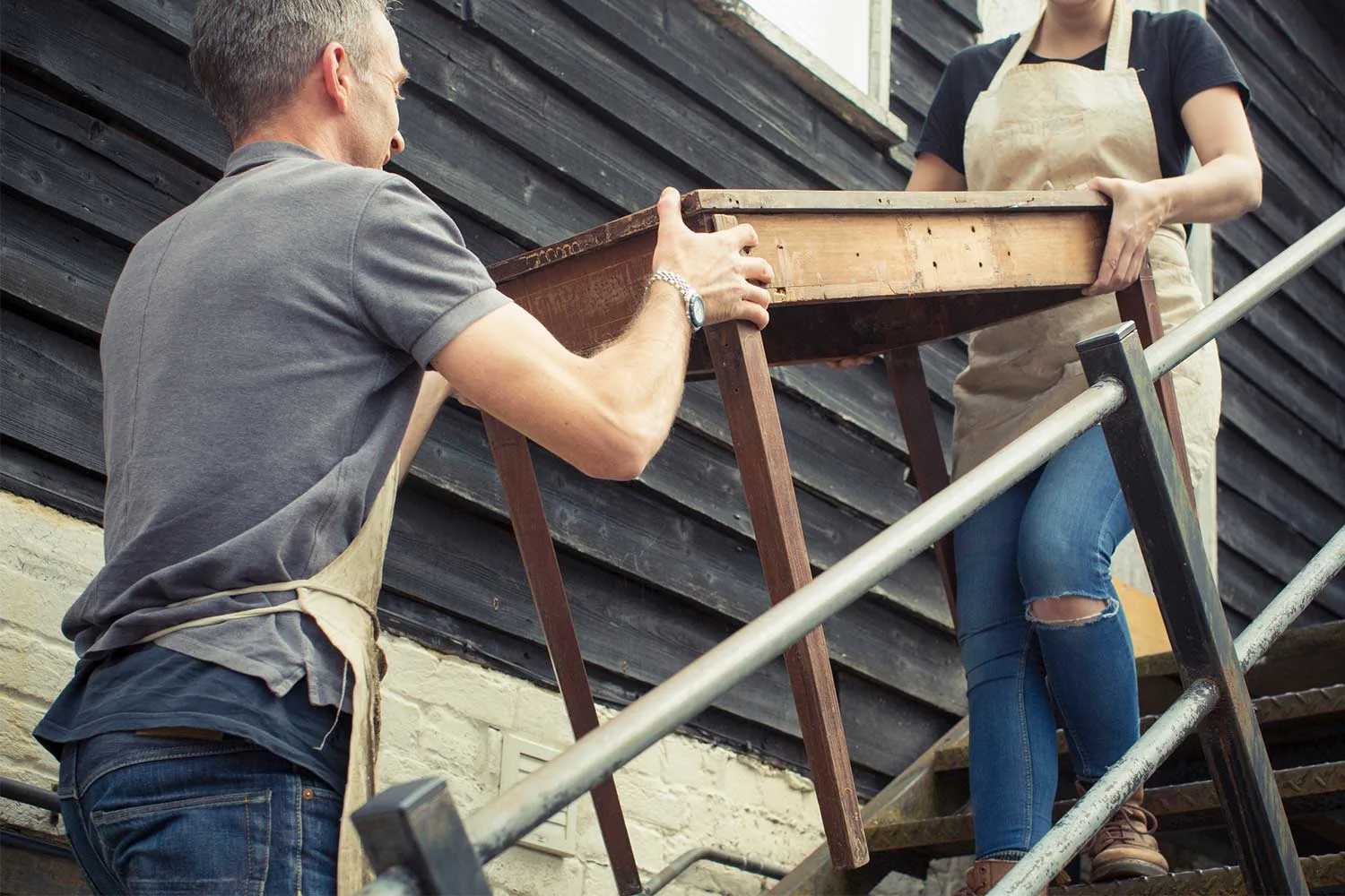 Man and woman lifting timber table up staircase