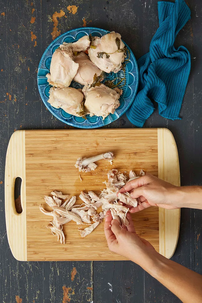 Shredding poached chicken on a wooden chopping board