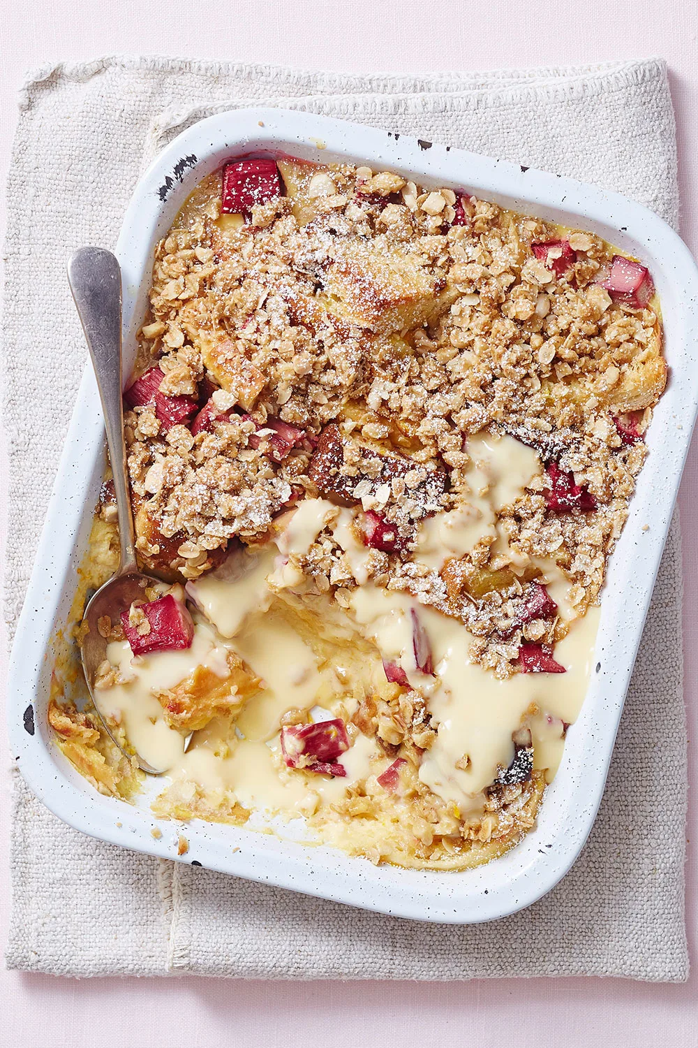 pie dish with custardy crumble and red fruit in it with icing sugar on top