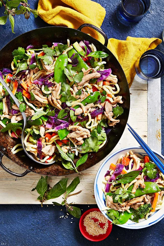 Chicken and lime stir fry with snow peas, red cabbage and sesame seeds on top in a circular cast iron pot with spoon on top.