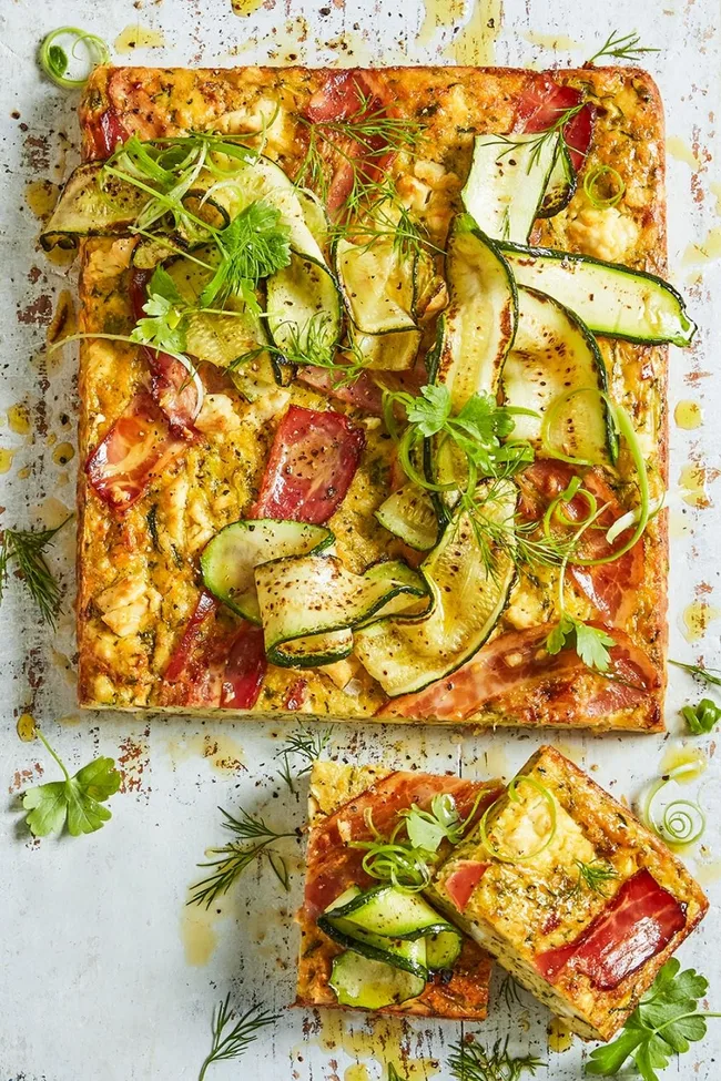 Zucchini slice with cooked zucchini ribbons and thin tomato slices, parsley and dill on top.