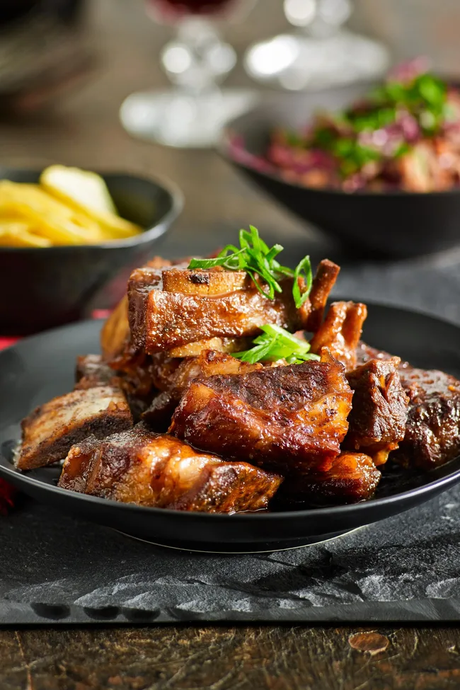 Slow-cooked beef ribs piled on top of each other with parsley in a black bowl