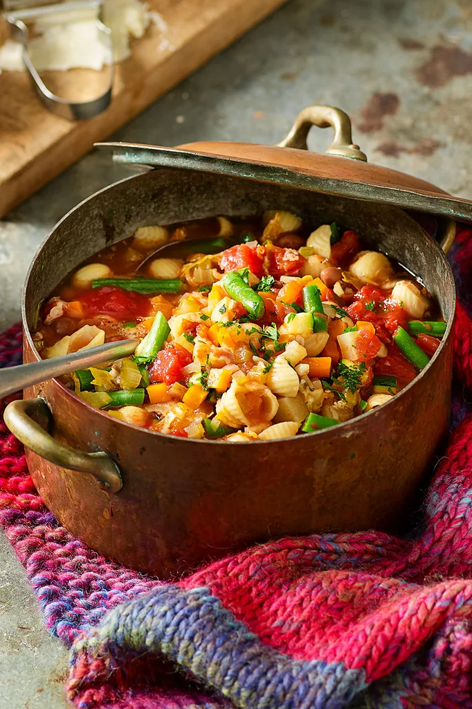 Minestrone soup with pasta and colourful vegetables in rusted cast iron pot with a spoon in it.