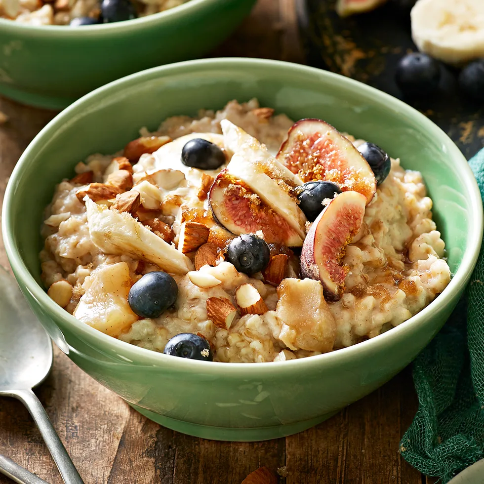 A bowl of overnight oats porridge in a green bowl topped with fresh blueberries, mixed nuts and figs