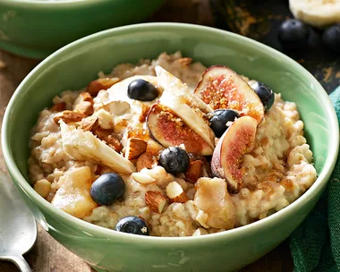 A bowl of overnight oats porridge in a green bowl topped with fresh blueberries, mixed nuts and figs