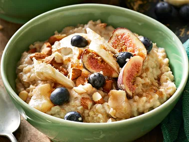 A bowl of overnight oats porridge in a green bowl topped with fresh blueberries, mixed nuts and figs