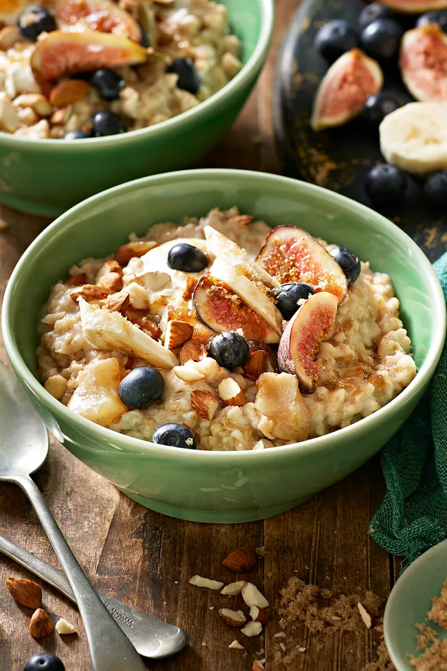 A bowl of overnight oats porridge in a green bowl topped with fresh blueberries, mixed nuts and figs