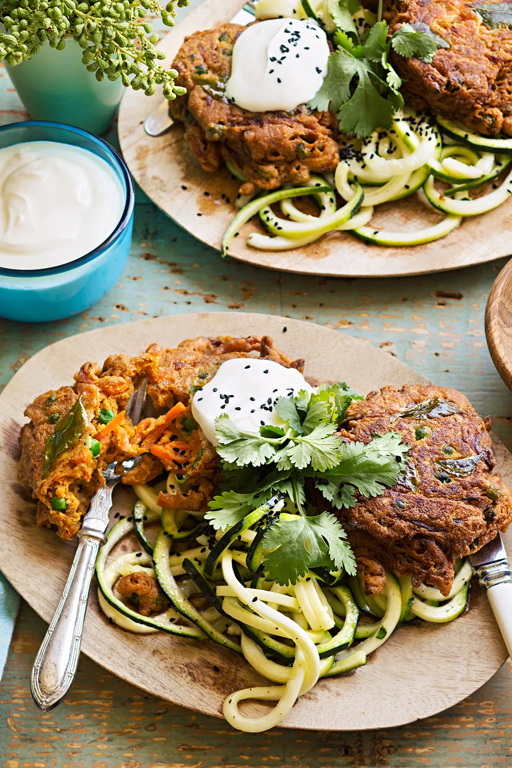 Spiced carrot and pea fritters with zucchini salad on wooden plate with black sesame seeds
