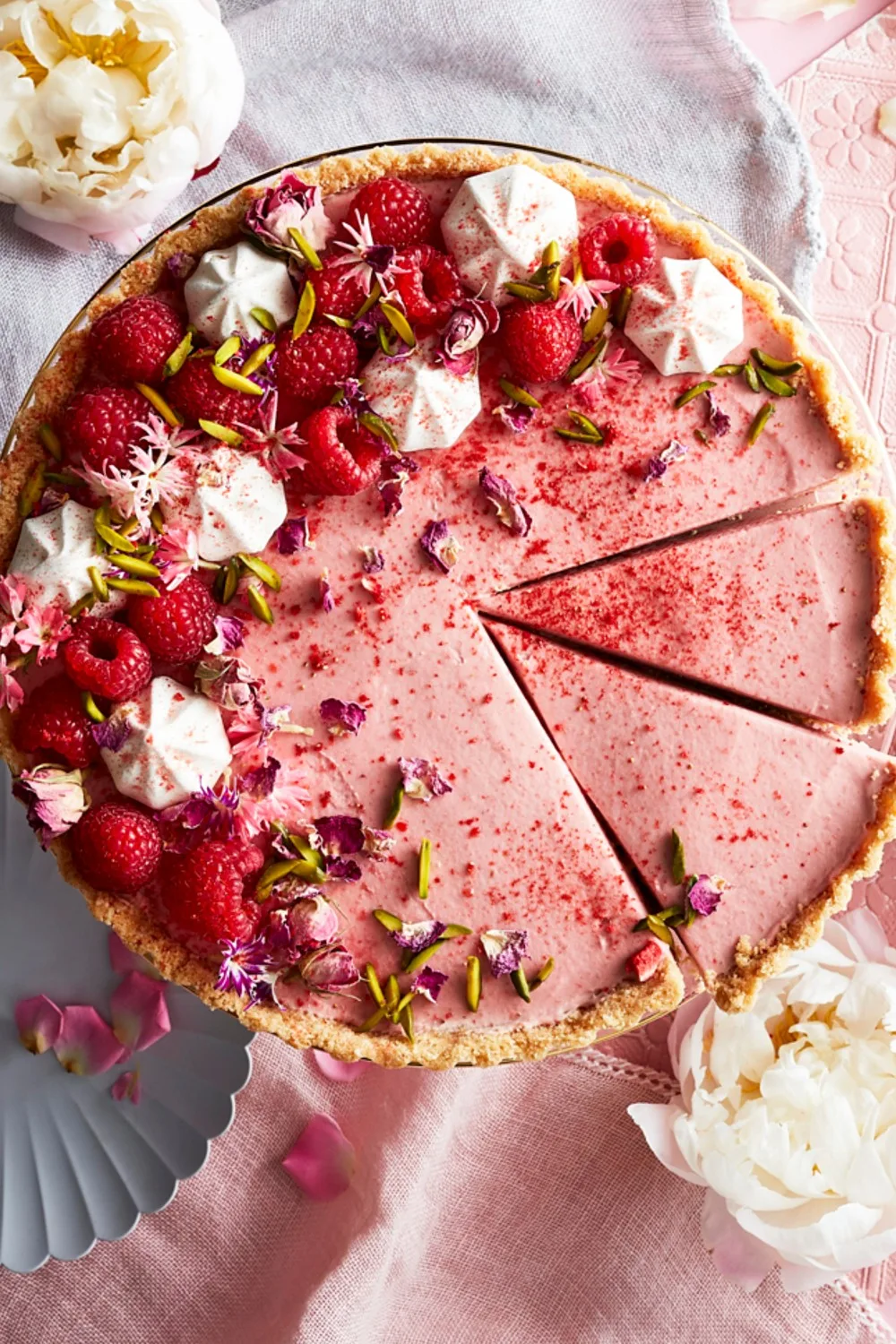 pink cake with dried rosebuds and raspberries on top. two slice cut into the cake