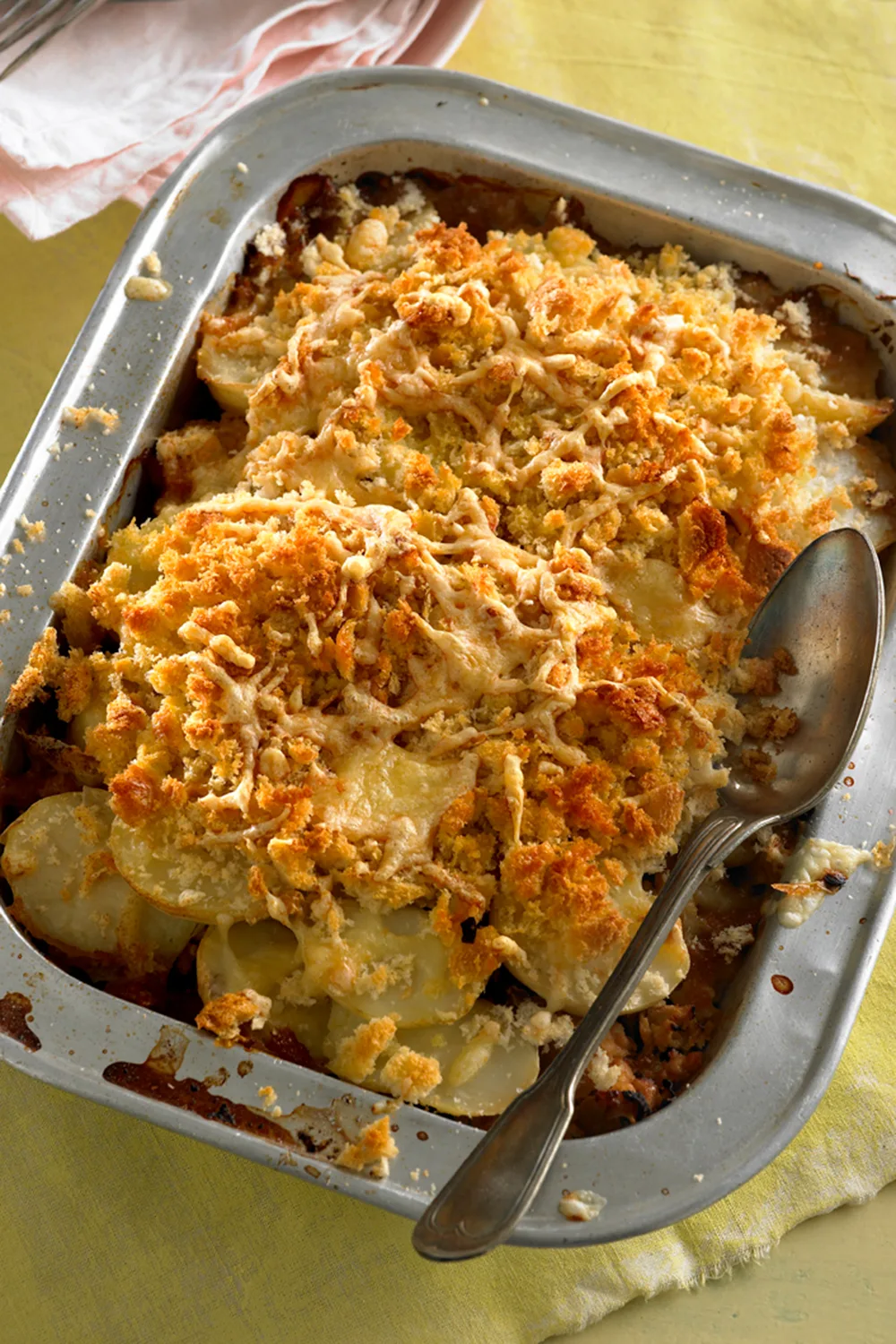 Chicken and potato bake in metal baking dish with breadcrumbs on top and spoon on the side