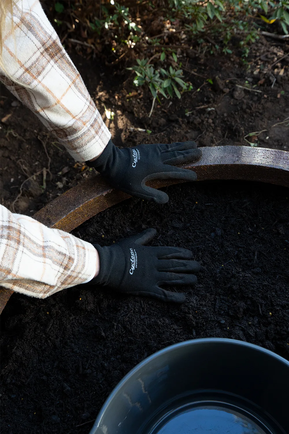 gloved hands pressing down fresh soil into pot plant