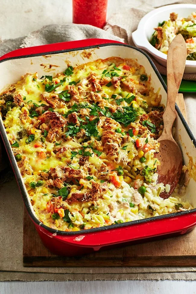 Tuna mornay with melted cheese and green herbs sprinkled on top in a red rectangular cast iron pot.