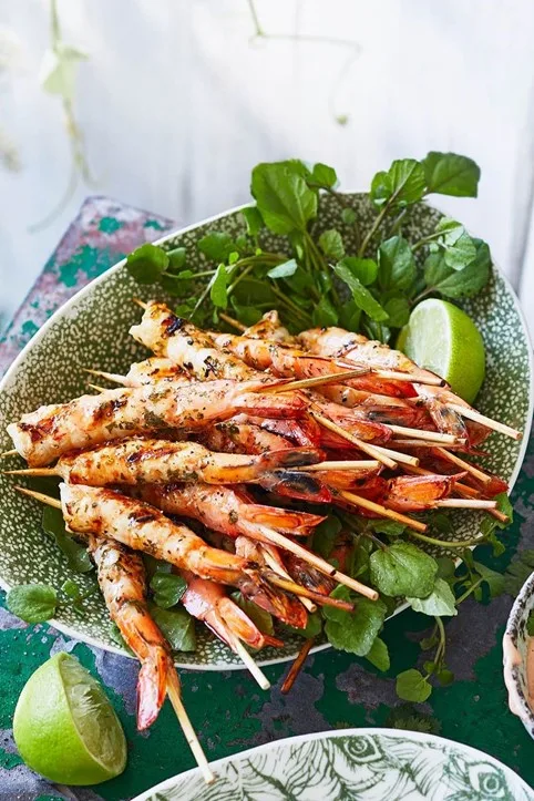 bbq marinated prawns in small pule with limes cut in half and fresh herbs underneath