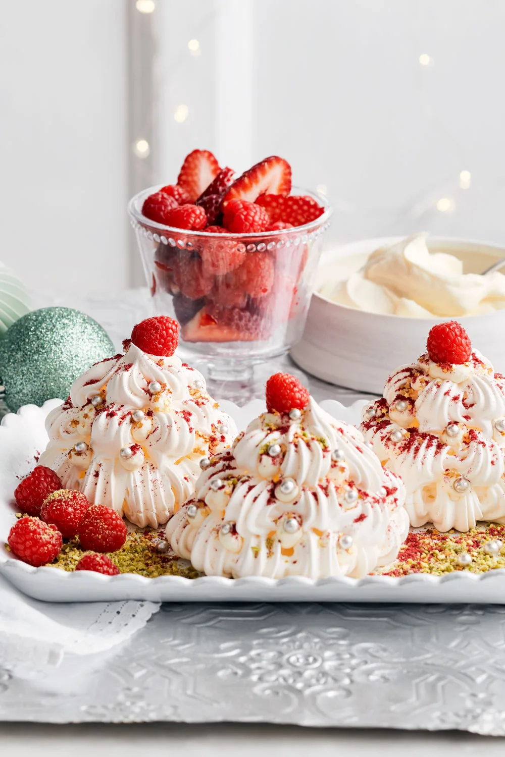 mini pavlovas in the shape of christmas trees with cashous and a raspberry on top