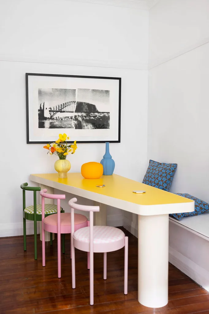 yellow table paired with coloured chairs pink green with black and white photo on the wall