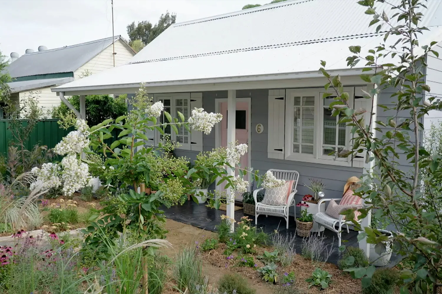 australian cottage garden in front of weatherboard house with pink door. 