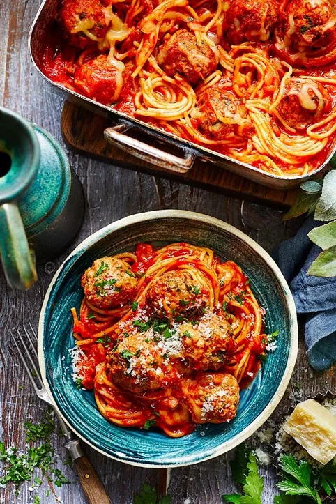 Spaghetti and meatballs bake in a blue bowl with sprinkled with a green herb garnish and Parmesan cheese.