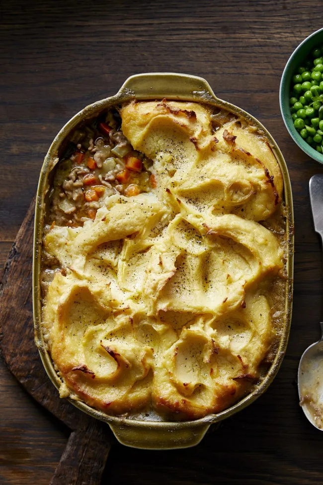 Shephard's Pie in a brown round rectangular dish with mashed potato on top. A gap from a missing slice shows the meat and vegetable contents of the pie.