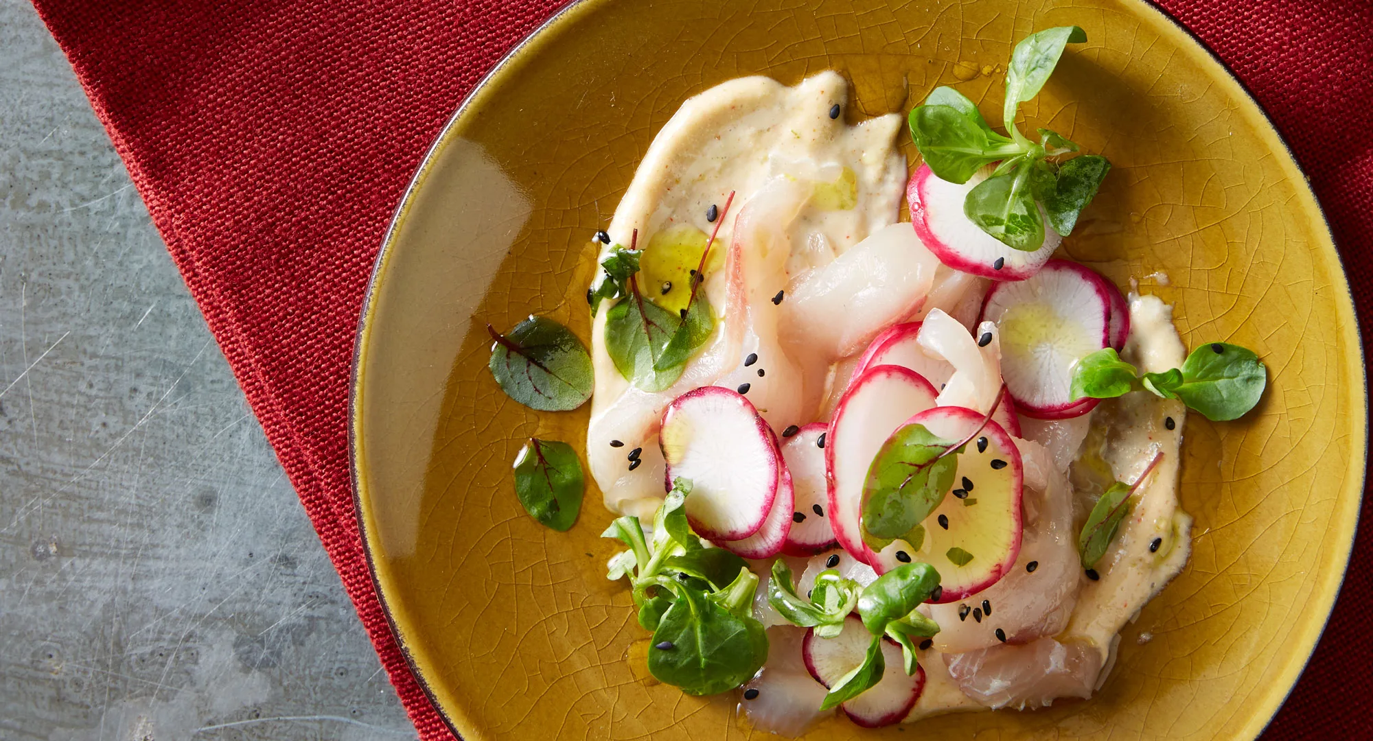 half image of kingfish tartare with shaved radish and sprouts on top