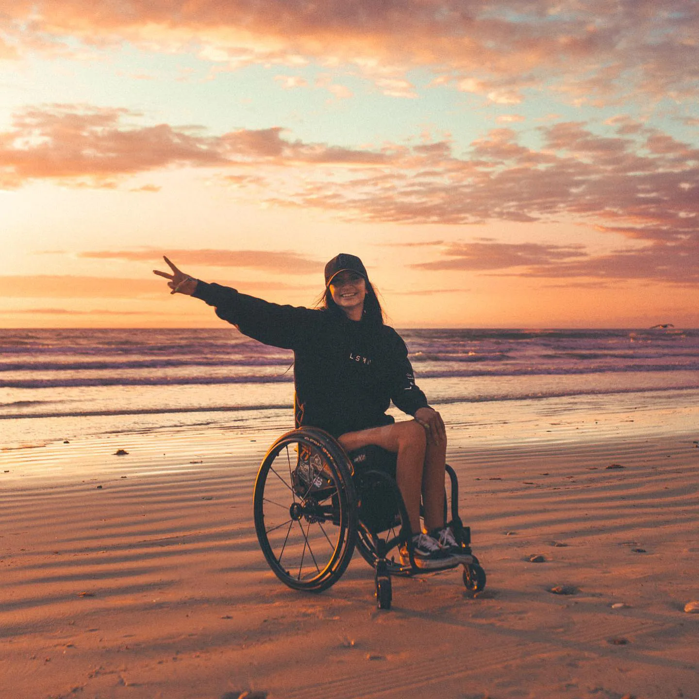 Woman paralysed from waist down using wheelchair posing for picture on the beach at sunset