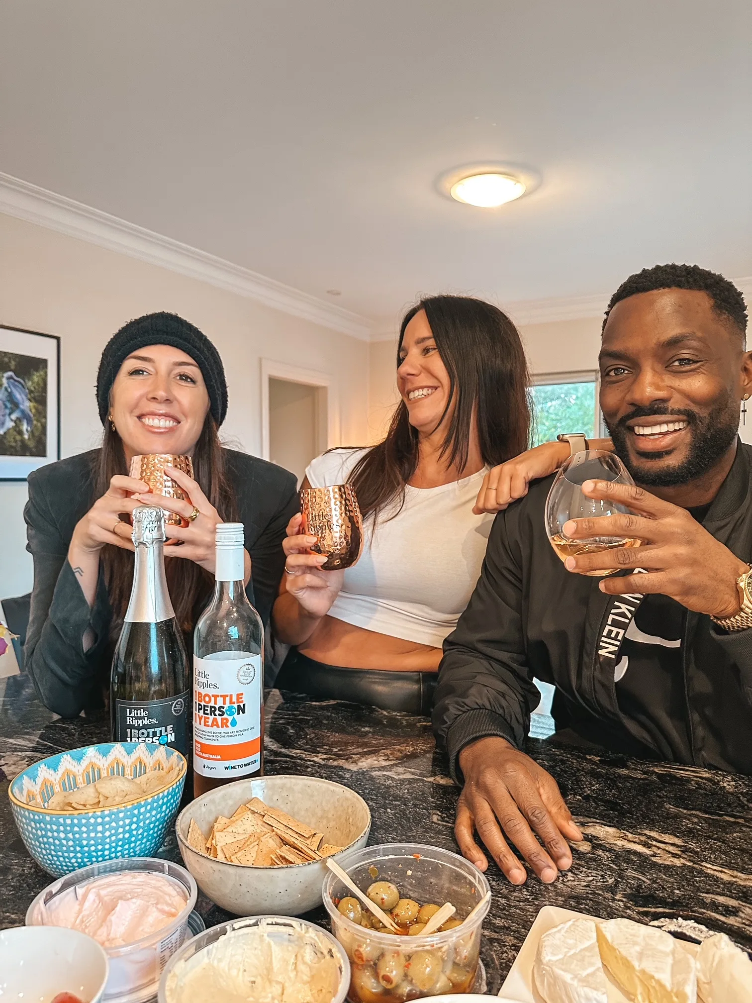 Two women and a man holding wine tumblers at a dining table with a tapas selection on it