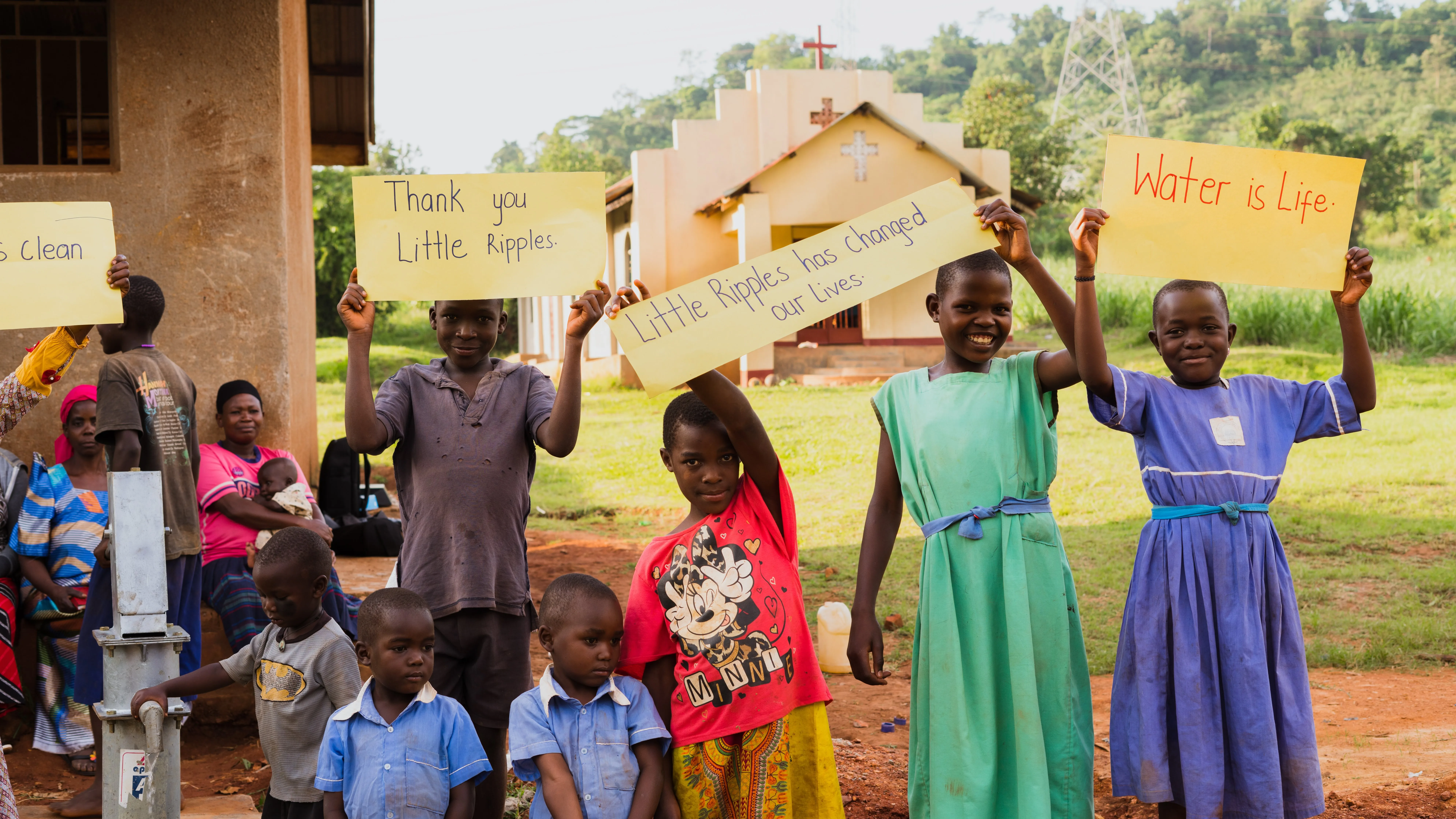 Children by a water pump in Africa holding thank you signs