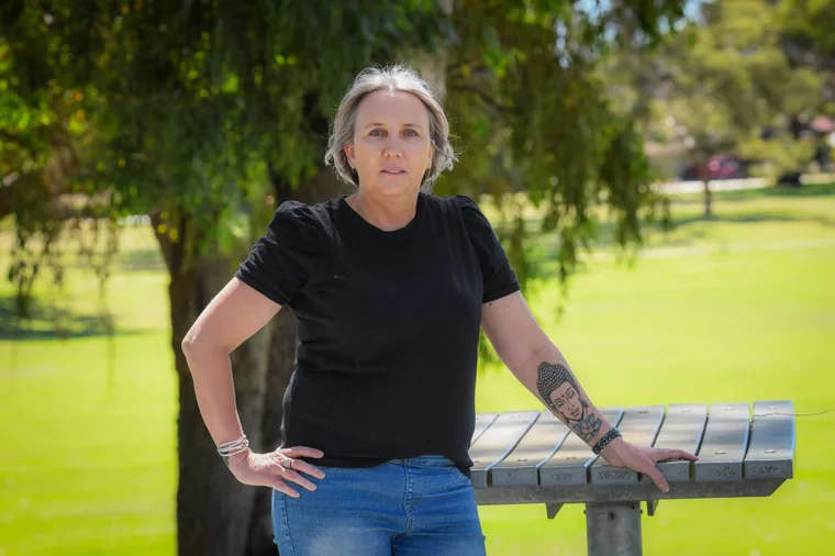 Woman standing outside by a bench in front of a park.