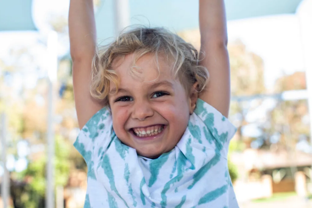 Photo of young boy with curly blond hair hanging from the monkey bars