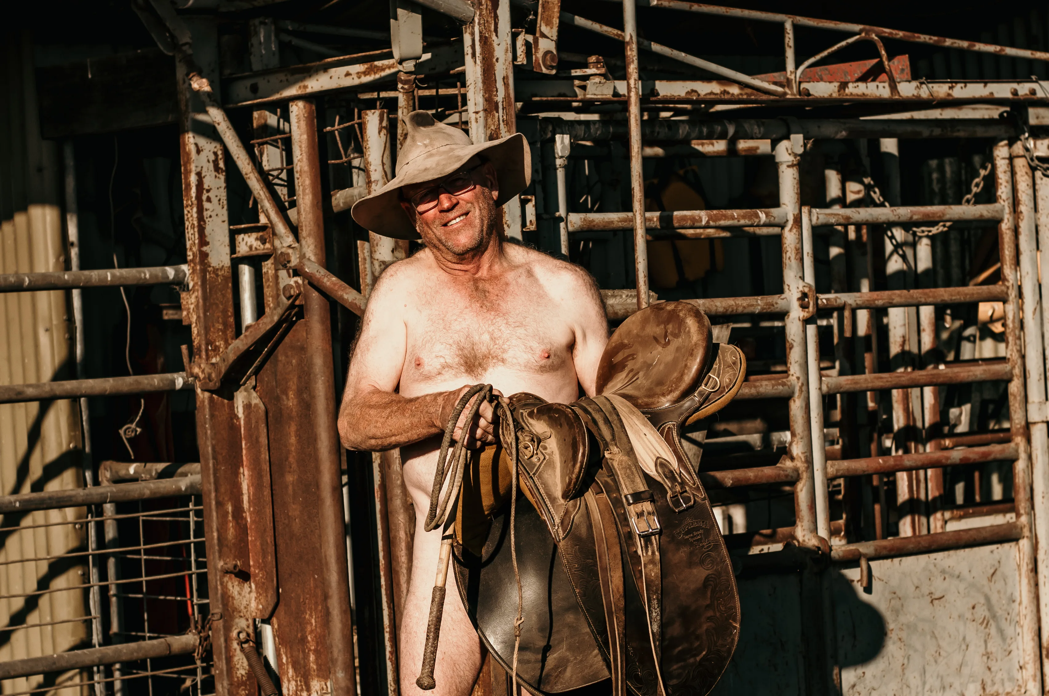 Image of man standing in the nude covered with a saddle