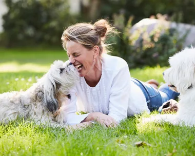 woman in white with two dogs laying on the grass