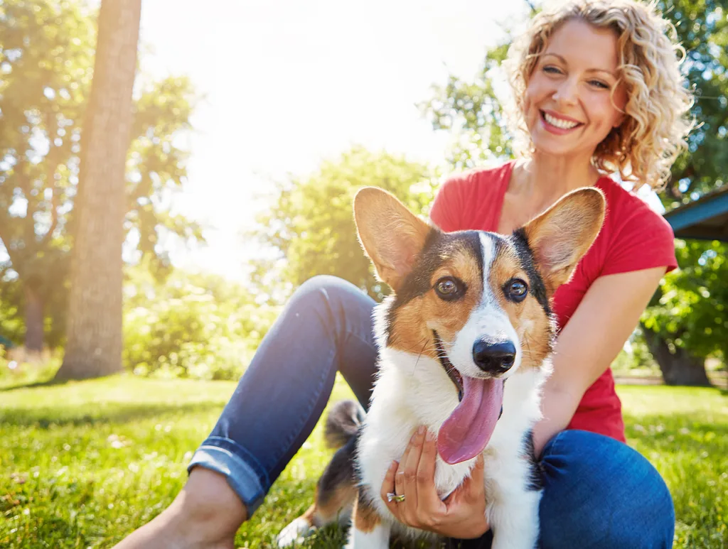 woman in red top sitting with dog on grass