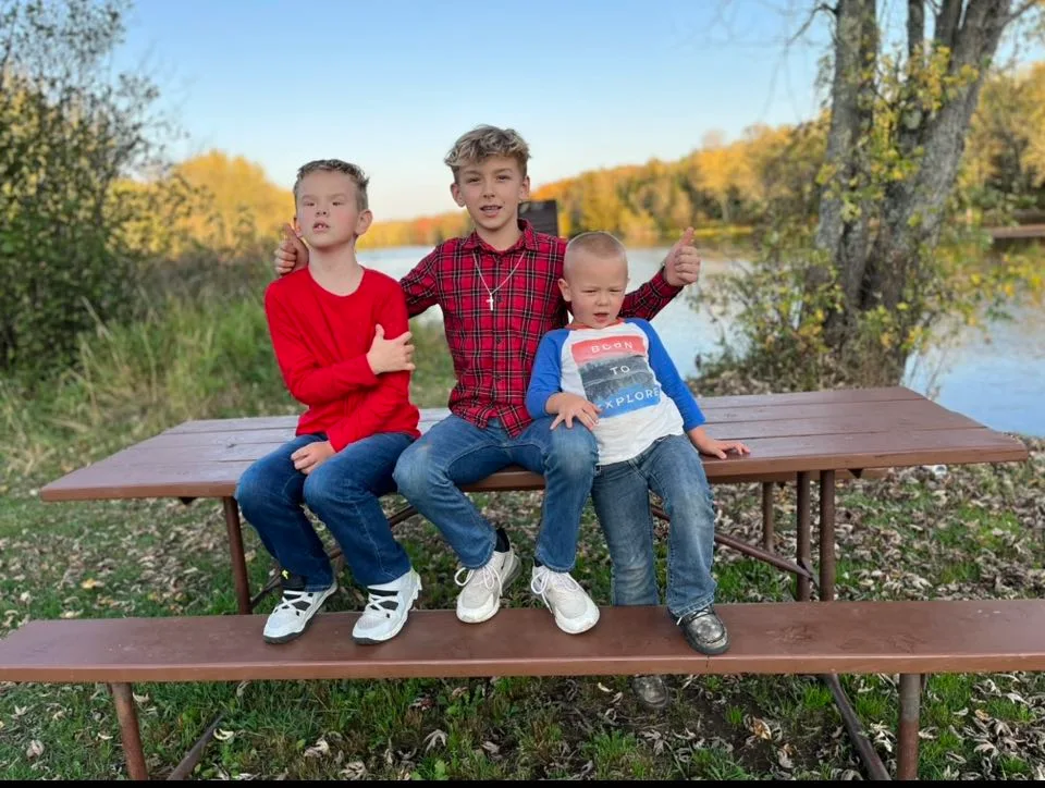 Three brothers are sitting on a picnic bench in front of a lake.