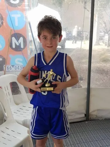Mac Holdsworth wearing a blue tshirt standing with trophies in front of chairs