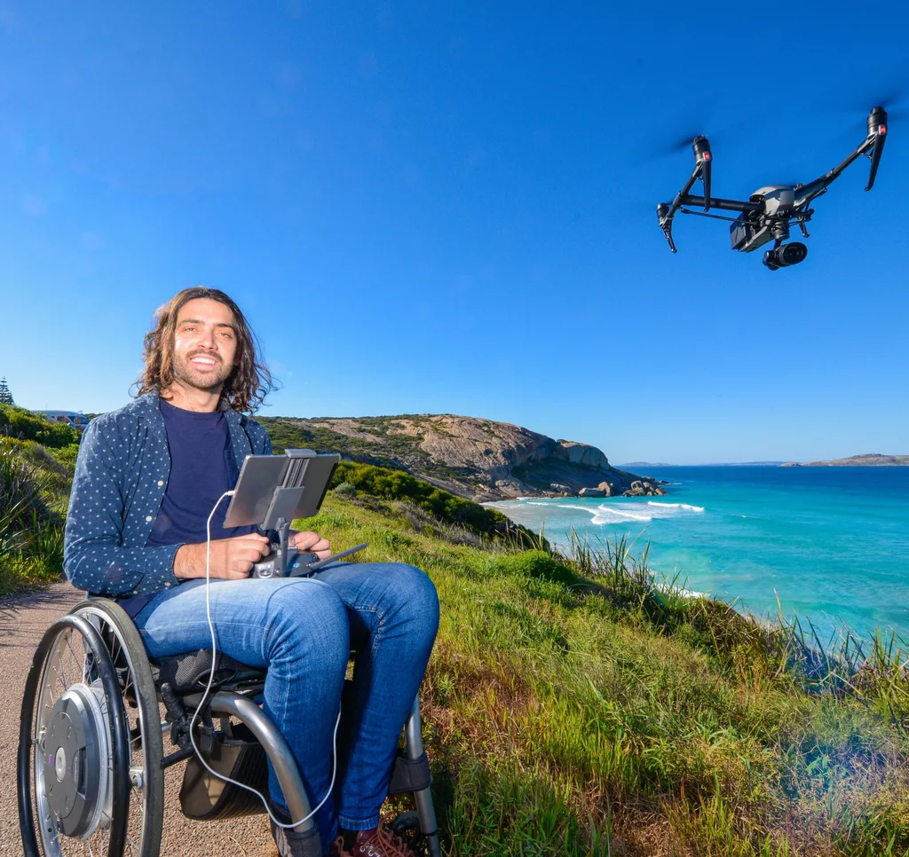 Main in wheelchair in front of sea with drone beside him