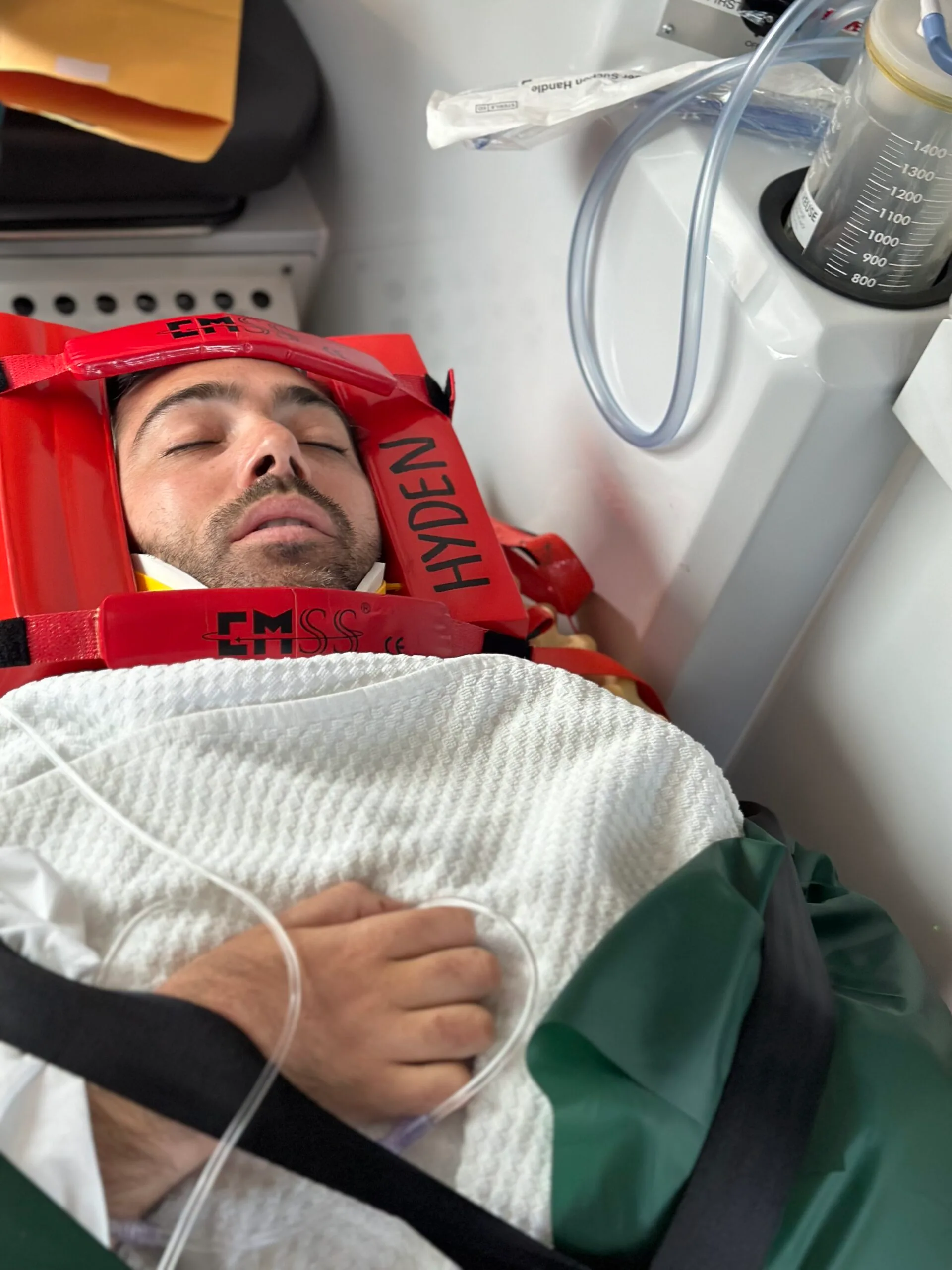 Man in red frame around head with white blanket and tube on way to hospital