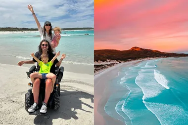 man in wheelchair with child on lap woman standing behind holding baby. Aqua blue water of Lucky Bay against Pink sky