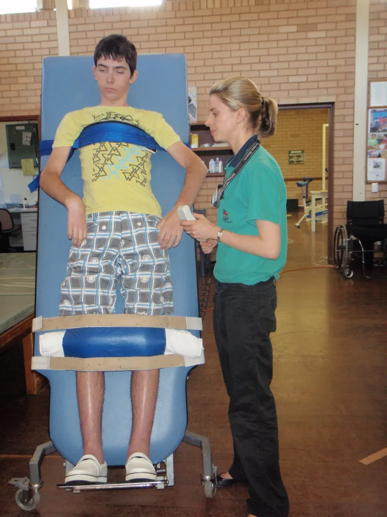 Young man strapped to board in yellow tshirt and shorts with woman in blue shirt stood next to him .